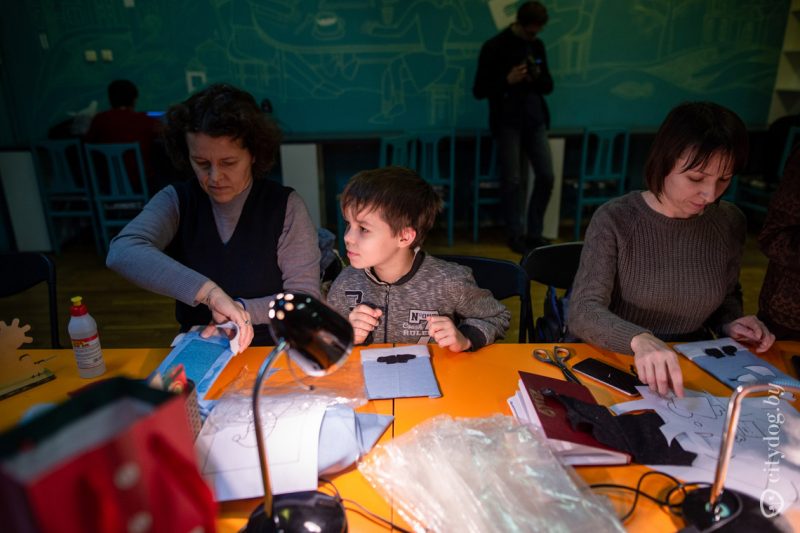 Маленькі хлопец і дзве жанчыны сядзяць за сталом і робяць тактыльныя кнігі