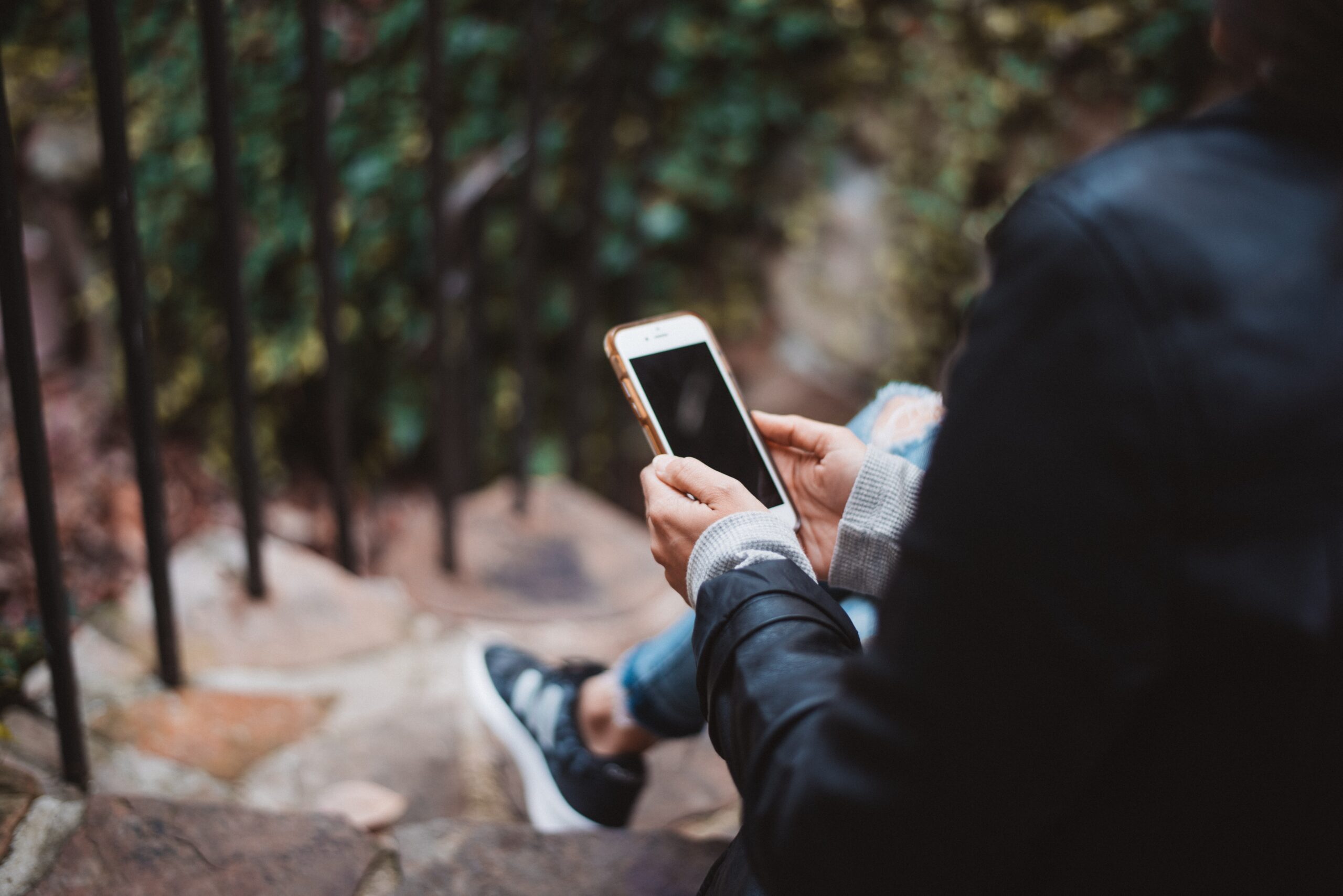 Женщина с телефоном в руках сидит на ступеньках в парке и собирается позвонить по телефону доверия