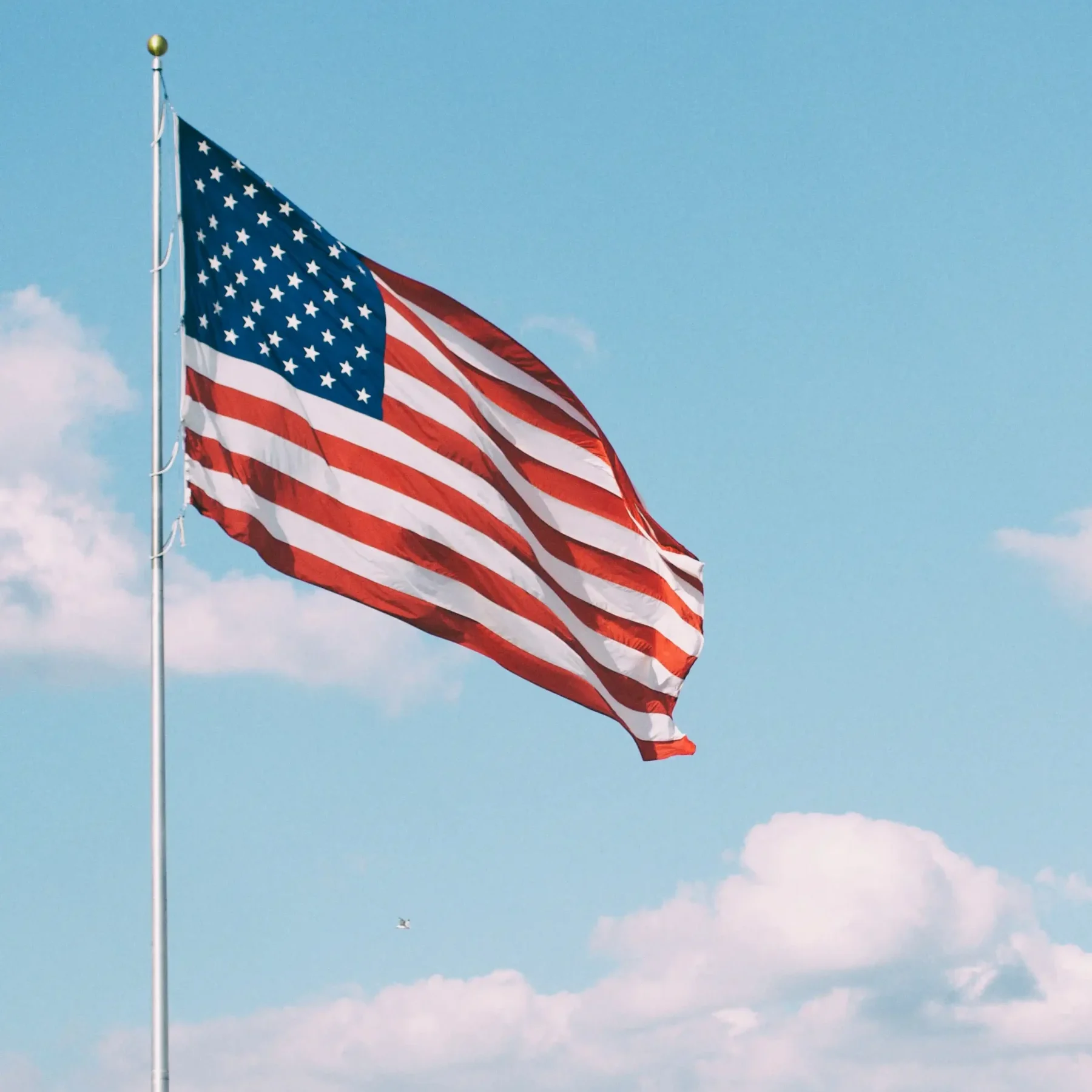 Амерыканскі сцяг на фоне блакітнага неба з белымі аблокамі